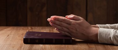 Kadın eli İncil 'de. Tahta masanın üzerinde İncil okuyup dua ediyor.