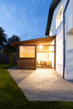 Avlu, veranda alanı, yeşil çimenler, bahçe ve akşamları araba olan modern beyaz evin dış görünüşü.