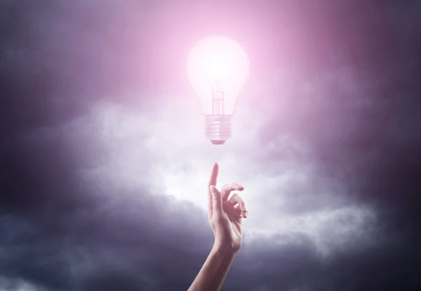 Woman hand reaching for light bulb — Stock Photo, Image