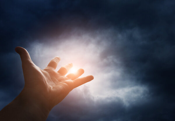 Hand reaching for the  sky with dark stormy clouds