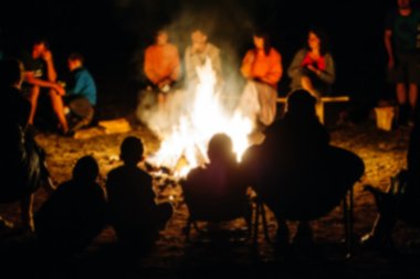 Blurred People sit at night round a bright bonfire clipart
