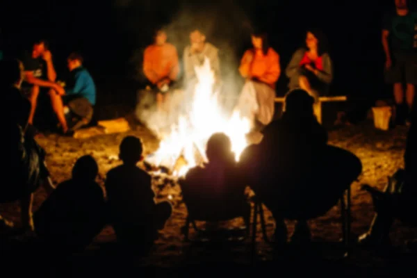 Blurred People sit at night around a bright bonfire — стоковое фото