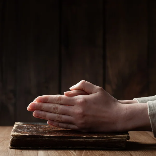 Руки женщины молятся с библией в темноте над деревянным столом — стоковое фото