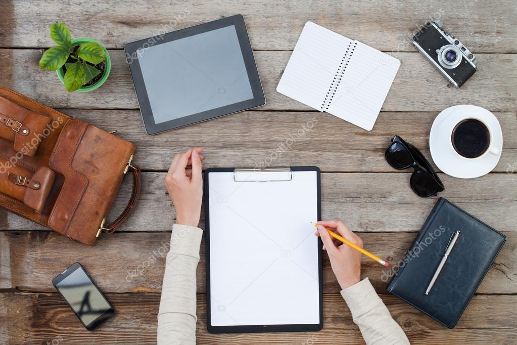 Woman's hand writing on paper with ipad style tablet and other items around