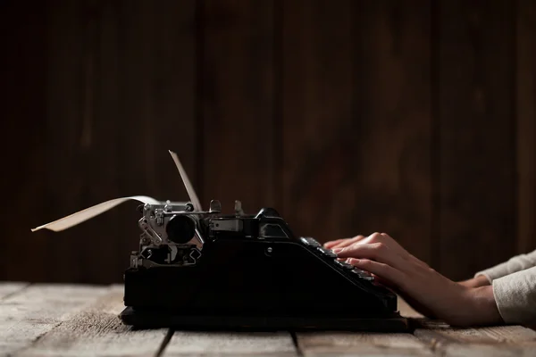 Manos escribiendo sobre una vieja máquina de escribir sobre un fondo de madera — Foto de Stock