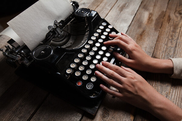 Hands writing on old typewriter over wooden table background