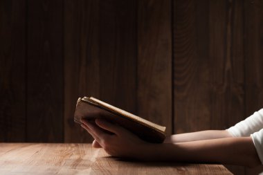 woman reading the bible in the darkness over wooden table clipart