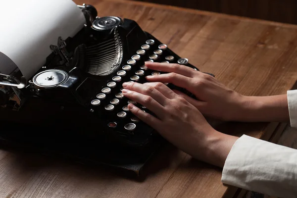 Manos escribiendo sobre una vieja máquina de escribir sobre un fondo de mesa de madera — Foto de Stock