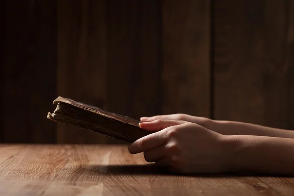 Mujer leyendo la Biblia en la oscuridad sobre mesa de madera — Foto de Stock