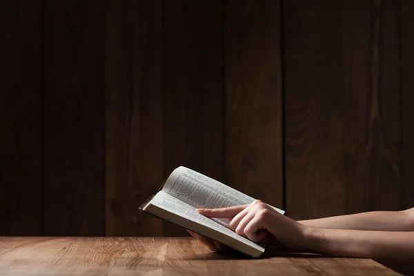 Женщина, читающая Библию в темноте над деревянным столом — стоковое фото