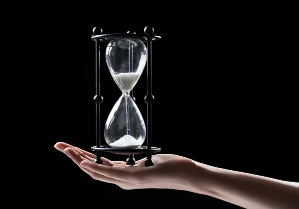 Hand met een zandloper zand horloge op zwarte achtergrond — Stockfoto