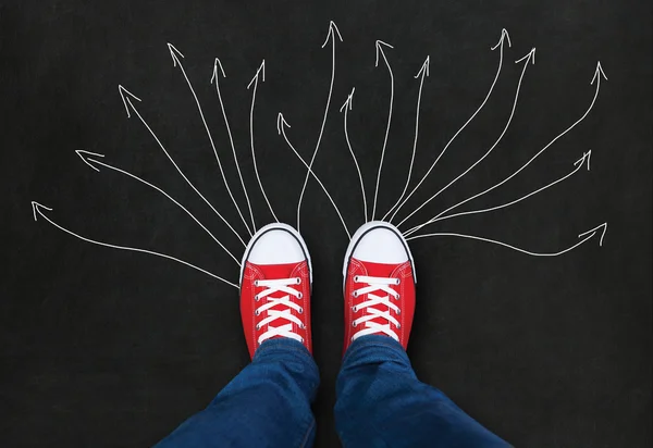 Feet wearing red shoes on black background with arrows. choice c — Stock Photo, Image