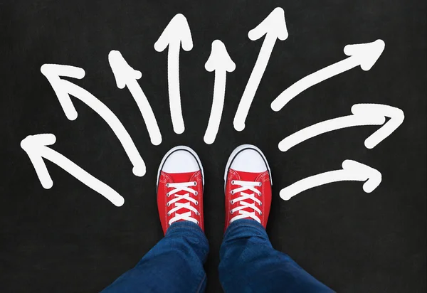 Feet wearing red shoes on black background with arrows in difren — Stock Photo, Image