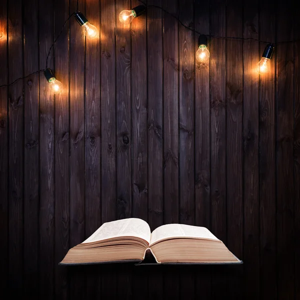 Livro aberto sobre um fundo de madeira com lâmpadas — Fotografia de Stock