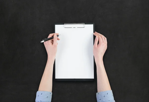 Hand holding pen with a blank note over blackboard background — Stock Photo, Image