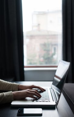 Tablet pc ve smartph içeren bir pencere yanında bir dizüstü bilgisayar kullanan kadın