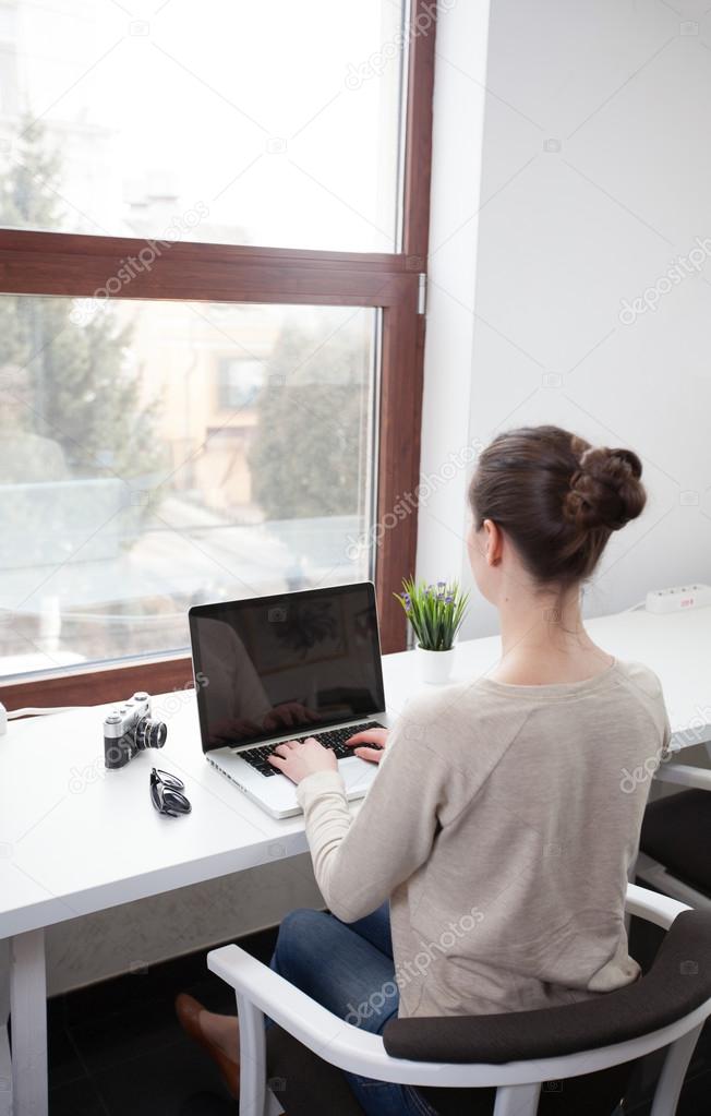 Woman using a laptop next to a window 