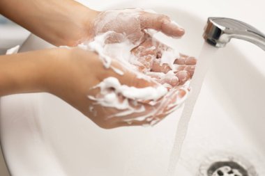 Banyoda, beyaz bir lavabo ve krom musluğun üzerinde bol köpüklü çocuk yıkama sabunu. Bakteri, virüs ve mikropların saflığı. Yakın plan fotoğraf.