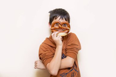 Genç bir çocuğun elinde iştah açıcı bir Bavyera krakeri. Krakeri maske olarak kullanarak kameraya bakıyor. Neşeli bir ruh hali. Fırın konsepti