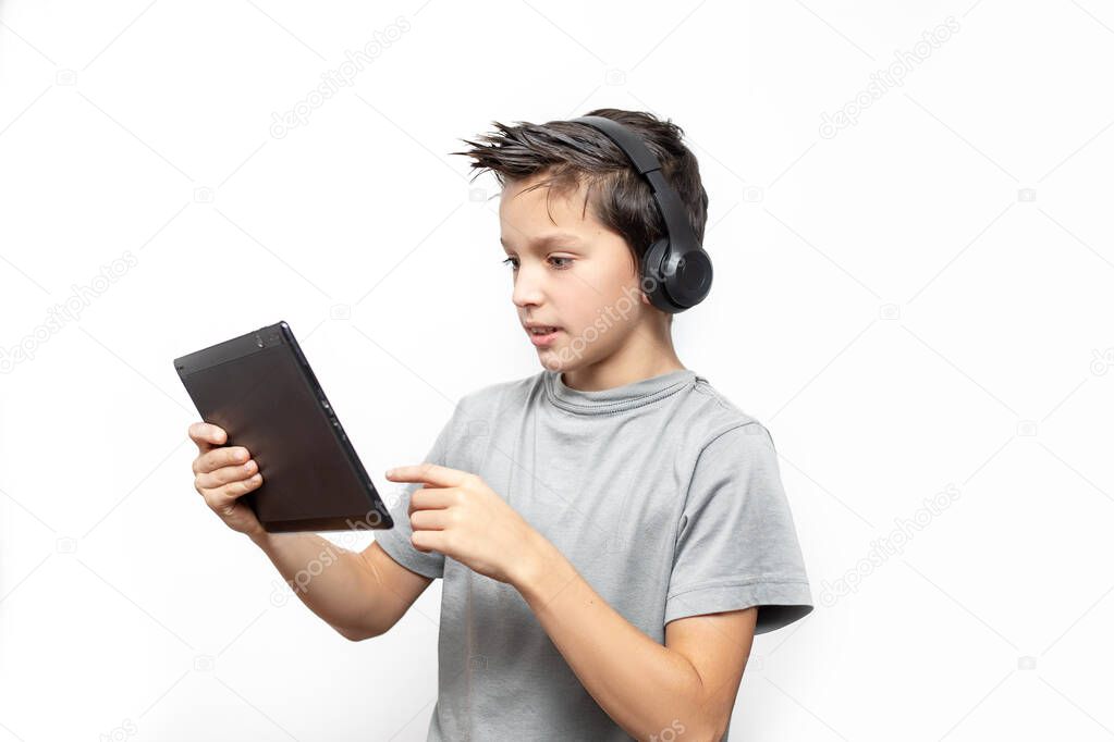 Video call and chat concept. Friendly teenage boy in headphones , conference calling on black digital tablet, white background. Digital education. Photo in studio