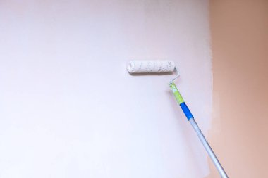 Boyacı, duvarda beyaz lekeli boya silindiri kullanıyor. Kapalı alanda fotokopi makinesi olan yakın plan fotoğraf.