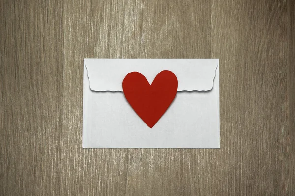 White envelope with red valentine heart on wooden background. Flat lay, close-up photo, mock up. Concept domestic life