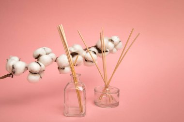 Reed difüzyoncuları pembe arka planda. Pamuk çiçekli oda parfümleri. Ev için hafif bir koku. Çiçek kokulu akromatik çubuklar. Ticari daire yatıyordu, ön manzarayla dalga geçiyordu. Aromaterapi parfümü