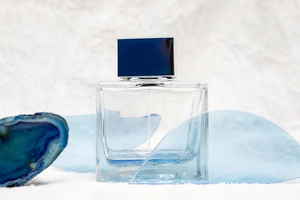 Glass bottle for men perfume or aftershave among abstract blue drifts on snow white background. Refreshing eau de toilette concept