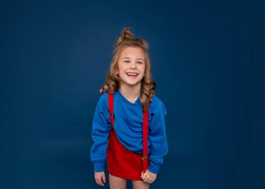 6-7 yıl boyunca heyecanla gülen sevimli bir kızın stüdyo portresi, mavi arka planda stüdyo çekimi. İnsan duyguları, yüz ifadeleri konsepti.