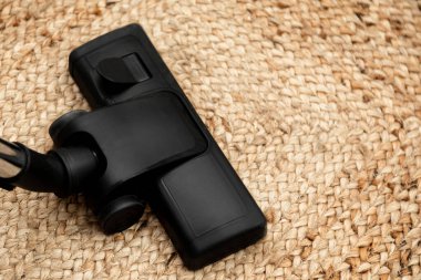 Kafanızı kapatın. Siyah elektrikli süpürge kullanılıyor. Kalın örgülü kahverengi halı süpürülüyor.