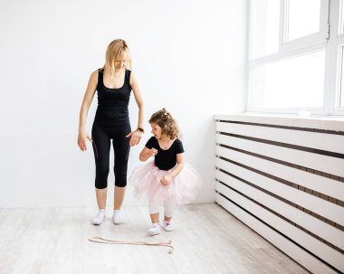 Anne, küçük kızıyla dans etmekten zevk alıyor. Beyaz bir iç mekanda jimnastik yapıyor.