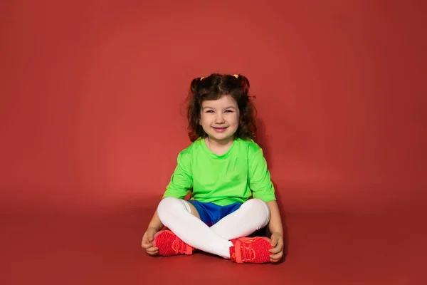 Stot Bambino Seduto Gambe Incrociate Sfondo Rosso Studio Uniforme Sportiva — Foto Stock