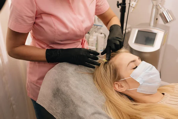 Injection against hair loss in head of blonde woman in clinic.