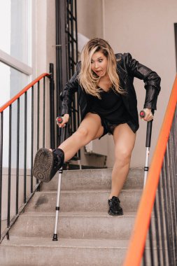 Koltuk değnekli genç bir kadın merdivenlerden düşüyor. Engelliler için yolcu asansörü yok. Espri fotoğrafı. Konsept kaza sigortası.