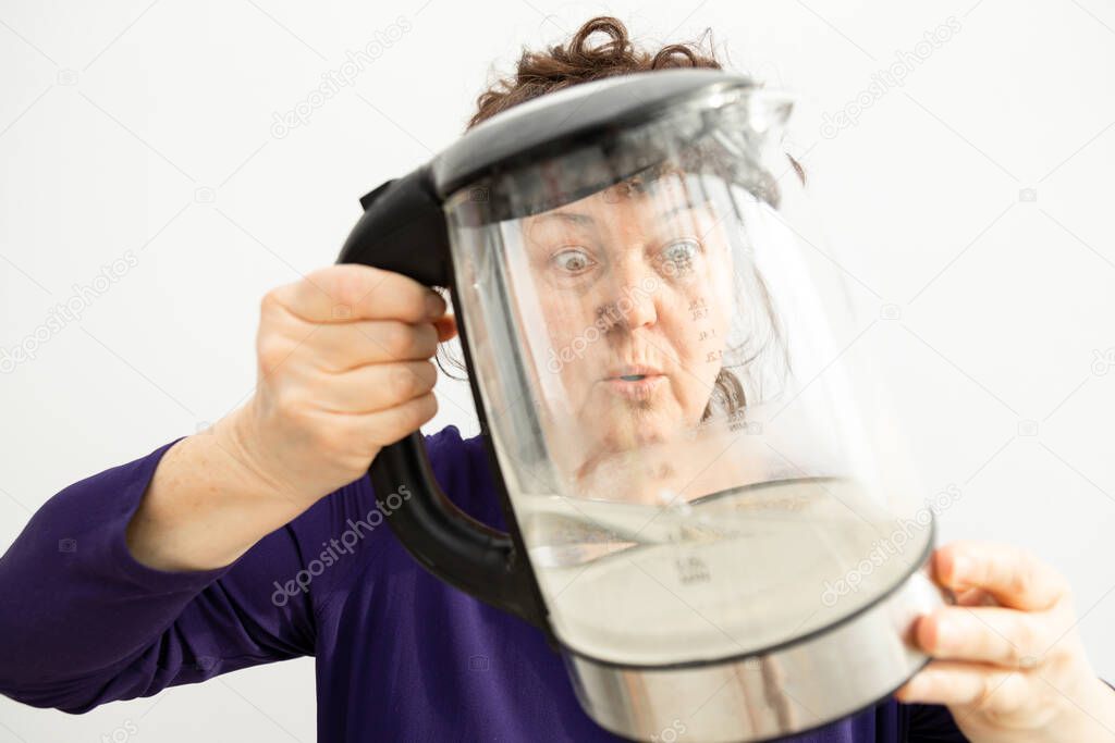 Woman looks through a transparent electric kettle with limescale. chalk residue of calcium carbonate. concept of repair of household appliances due to hard water.