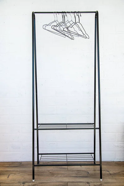 Stainless steel clothes rail with empty coathangers against a white wall, wooden floor.