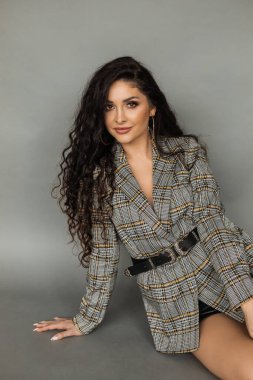 29 yaşındaki bir kadın gri arka planda oturuyor ve çerçeveye bakıyor. Uzun kıvırcık saçları ve anlamlı makyajı vardı. güzellik konsepti.