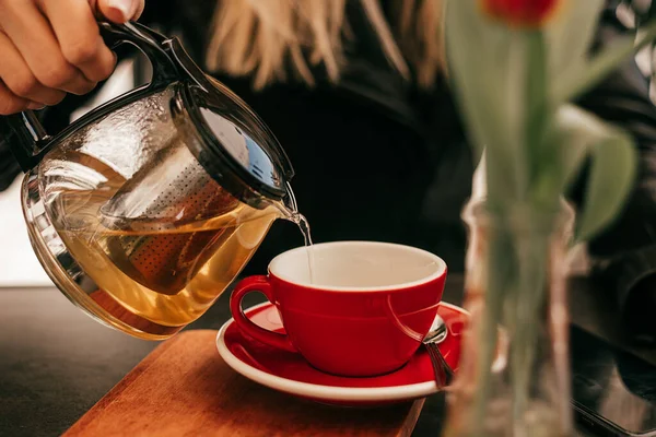 Woman\'s hand pours tea from glass teapot into cup in street cafe