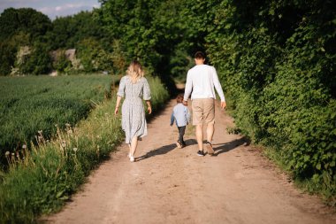Mutlu aile eğleniyor ve kır yolunda yürüyor, el ele tutuşuyor, dikiz manzaralı fotoğraf çekiyor.