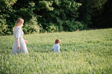 Genç anne oğluyla yeşil çimlerin arasında yürüyor. 3 yaşında.