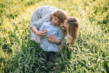 Anne 3 yaşındaki oğluna nazikçe sarılıyor, yaz günü tarlada yürüyorlar.