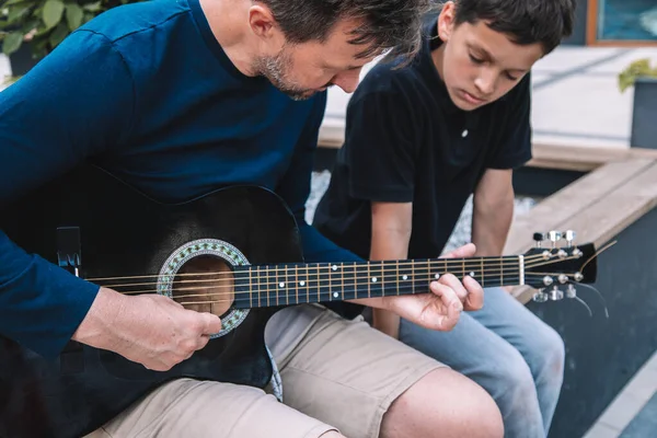 息子は父からギターを学ぶが 夏の日は市の広場に座る ライフスタイル — ストック写真