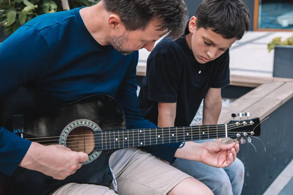 都会の広場で夏休みにギターを弾くことを息子に教える ライフスタイル — ストック写真