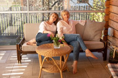 55 yaşındaki güzel bayanlar masadaki kanepede otantik bir ahşap evdeki çiçeklerle rahatsız olur.