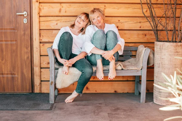 İki olgun kadın ahşap evin yanındaki bankta oturur ve zor bir günün ardından dinlenir, hayat tarzı fotoğrafı.