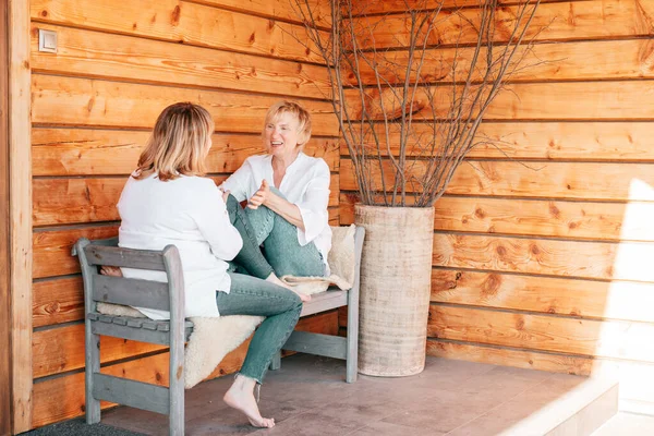 Ahşap evin arka planında sohbet eden iki yaşlı kadın.