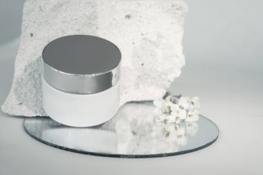 Krema kutusu beton parçasının üzerinde. Betonun gözenekli yapısı insan derisinin dokusuyla ilişkilidir. Kompozisyon bir ayna kullanır, narin bir çiçek. Tıbbi kozmetik konsepti