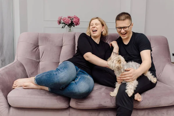 ピンクのソファにペットと一緒にリビングルームの若いカップルは楽しいです 休息とリラクゼーション 美しさと健康 家庭生活 現代の生活 — ストック写真