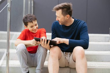 Baba ve oğul kentteki beton basamaklarda otururken tablet kullanarak yeni oyunu tartışırken iyi eğlenceler.
