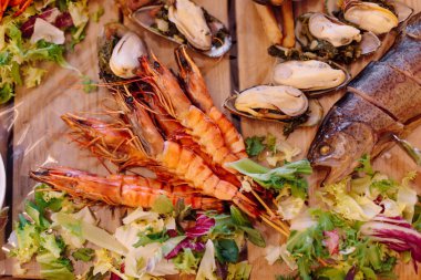 Midye, yengeç, salata ve ahşap tabakta limon dilimleri ile süslenmiş fırında balık. Restoranda şenlik yemekleri. Dinlenme ve turizm. Ziyafetler ve resepsiyonlar. Balık büfesi.